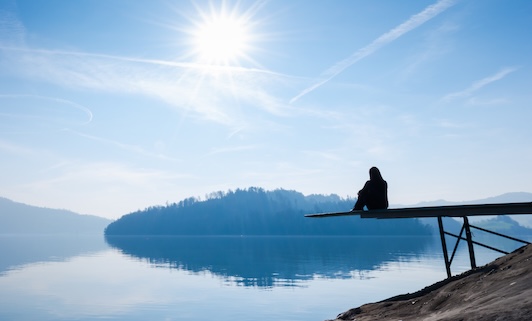 The woman is sitting on the pier. Self reflection. Bright sun in the blue sky.