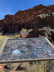 Interpretive sign and ancient stone walls at Citadel Pueblo in northern Arizona beneath a clear blue sky.
