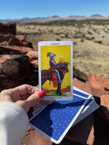 Knight of Pentacles tarot card held in front of the stone ruins of Citadel Pueblo in Arizona, symbolizing patience, stewardship, and building a lasting legacy.