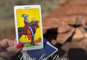 Knight of Pentacles tarot card held in front of the stone ruins of Citadel Pueblo in Arizona, symbolizing patience, stewardship, and building a lasting legacy.